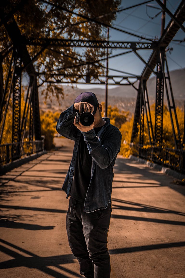 A man takes a photo on a bridge surrounded by autumn leaves.