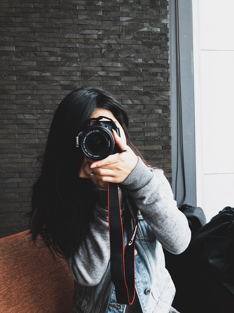 Asian woman holding a camera for a photoshoot indoors. Capturing creativity.