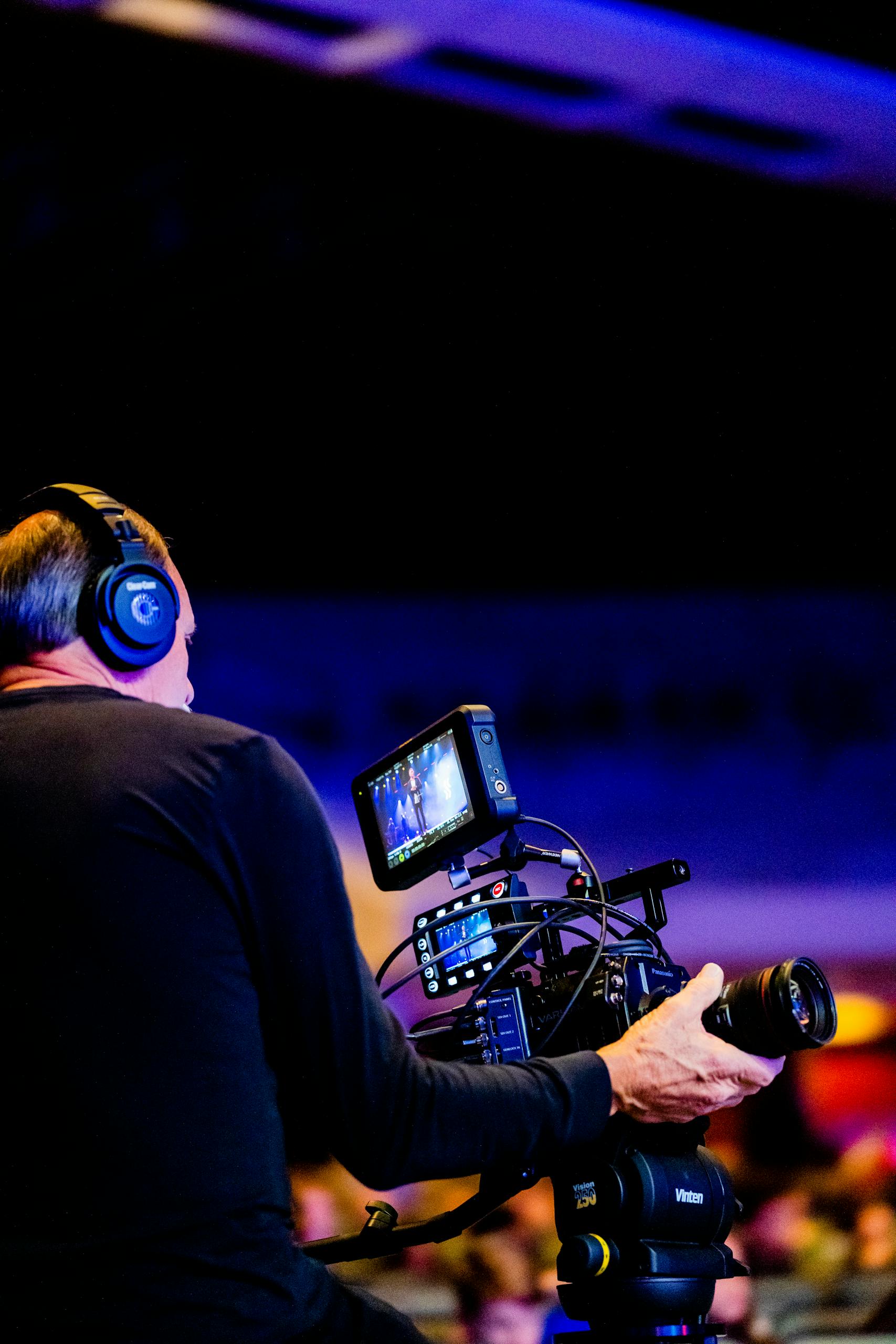 Cameraman with headphones operating a professional video camera indoors.