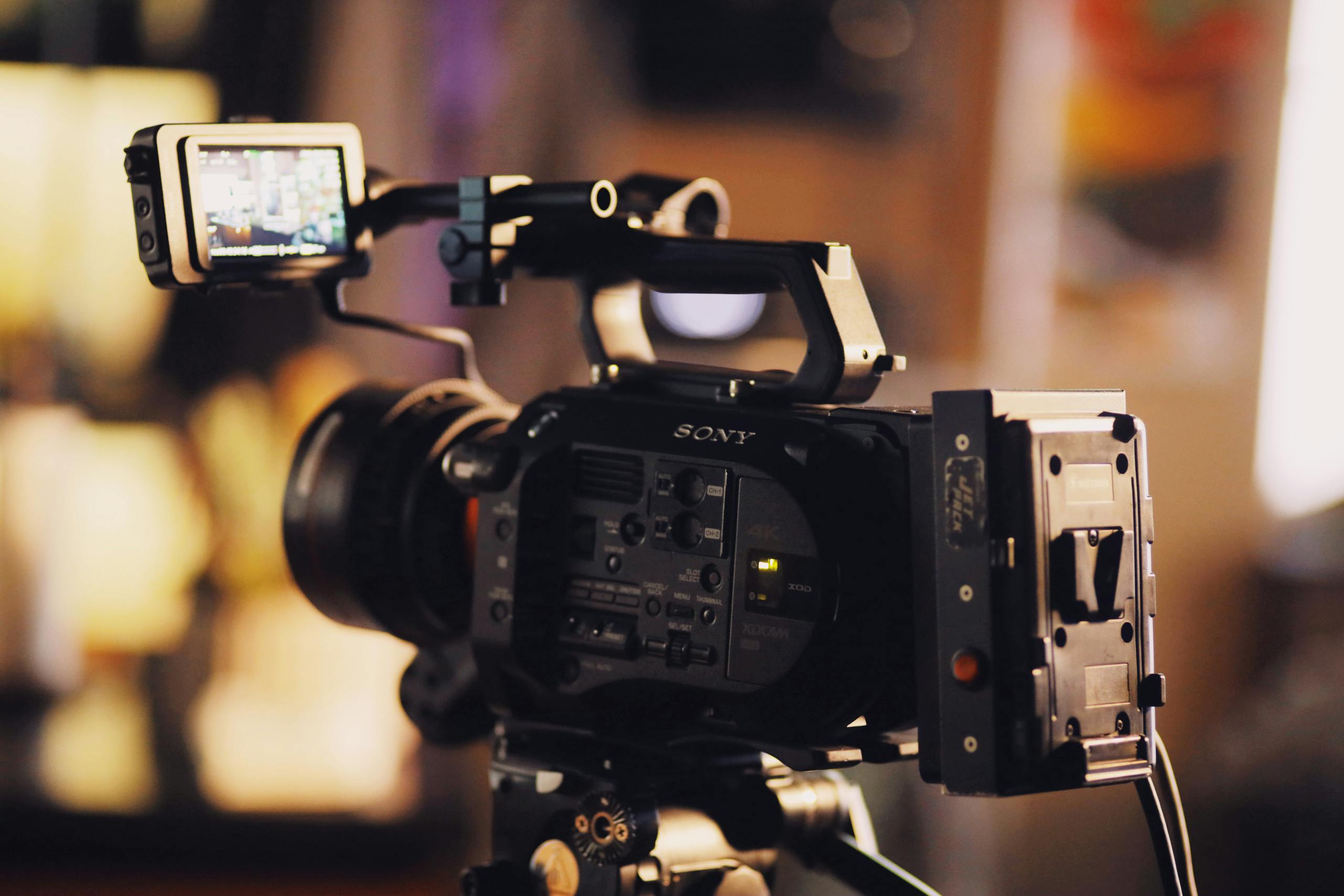 A modern video camera on a tripod with a small screen, perfect for filmmaking and video production.