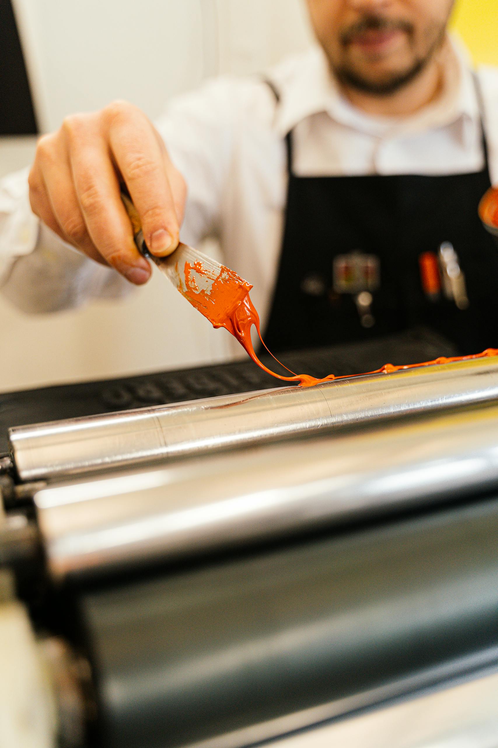An artisan skillfully applies red paint onto a metal roller, showcasing craft and technology.